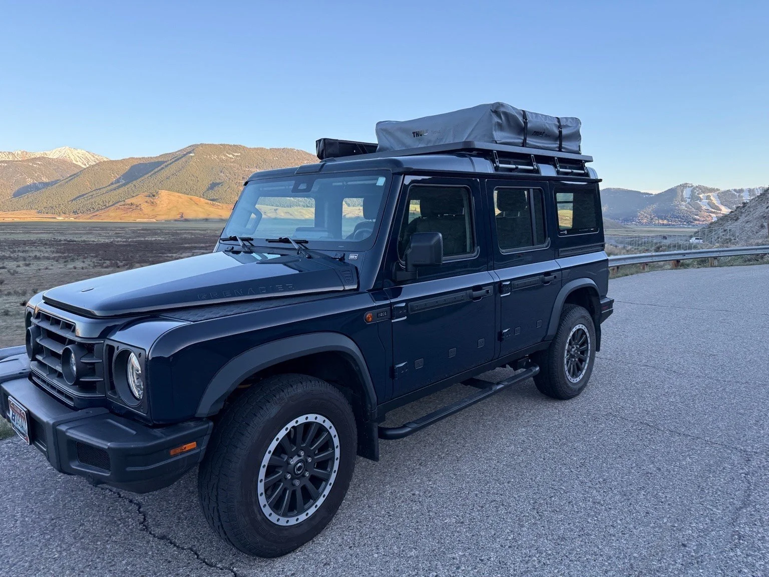 Black Mercedes-Benz G-Class SUV with roof cargo box parked on the side of a road in a mountainous landscape.