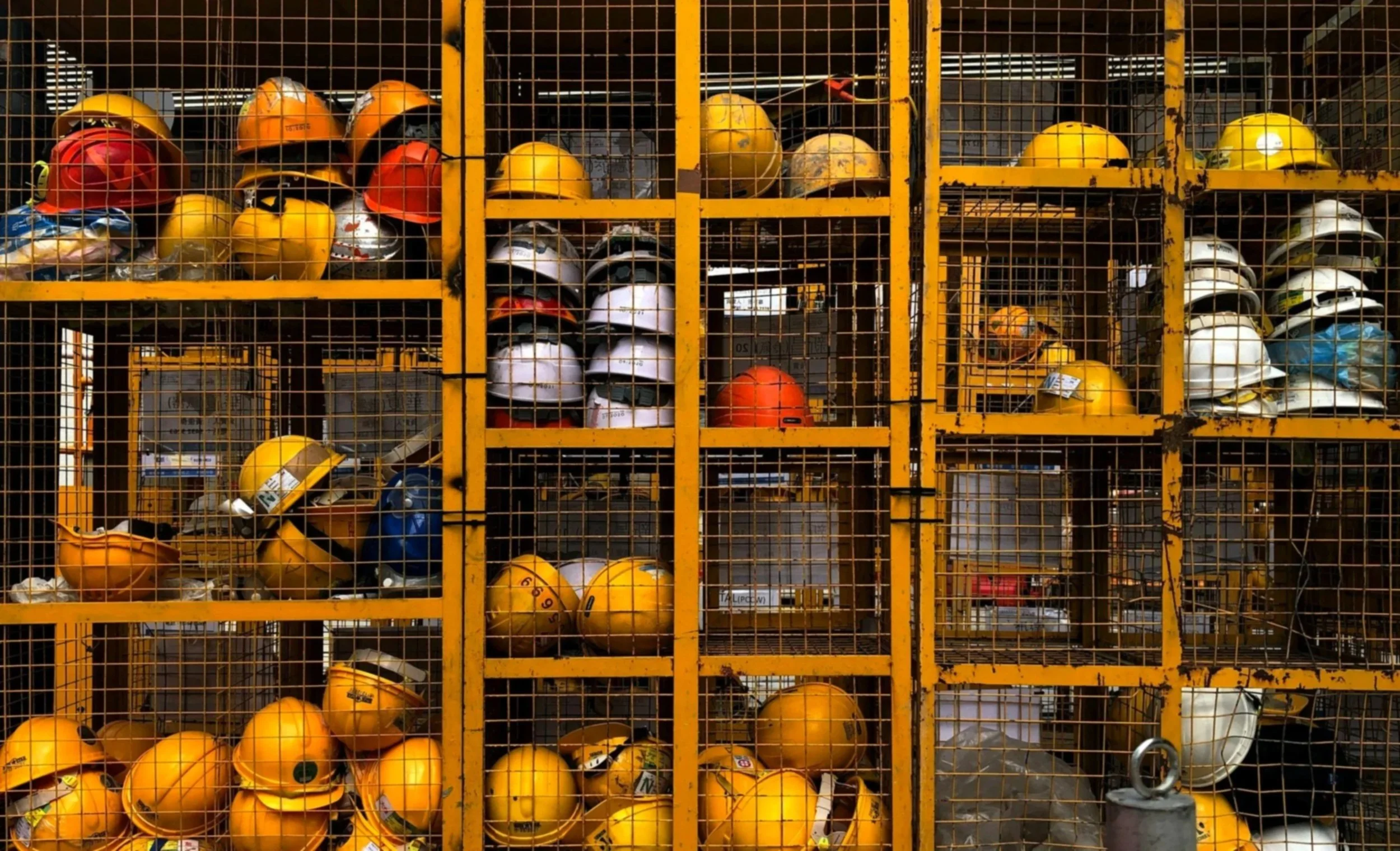 Storage of safety helmets in yellow metal cages, with the helmets in various colors including yellow, white, red, and blue, arranged on shelves.