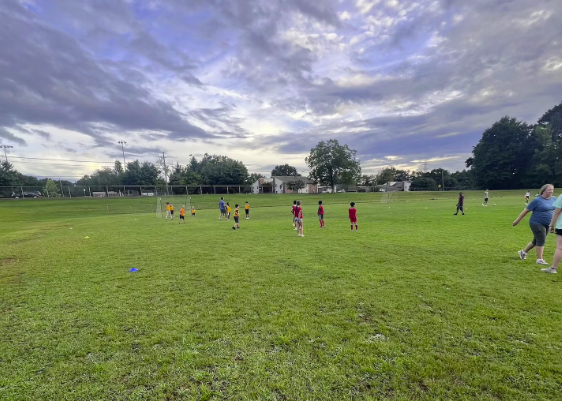 Soccer practice on a grassy field with children and adults, under a cloudy sky.