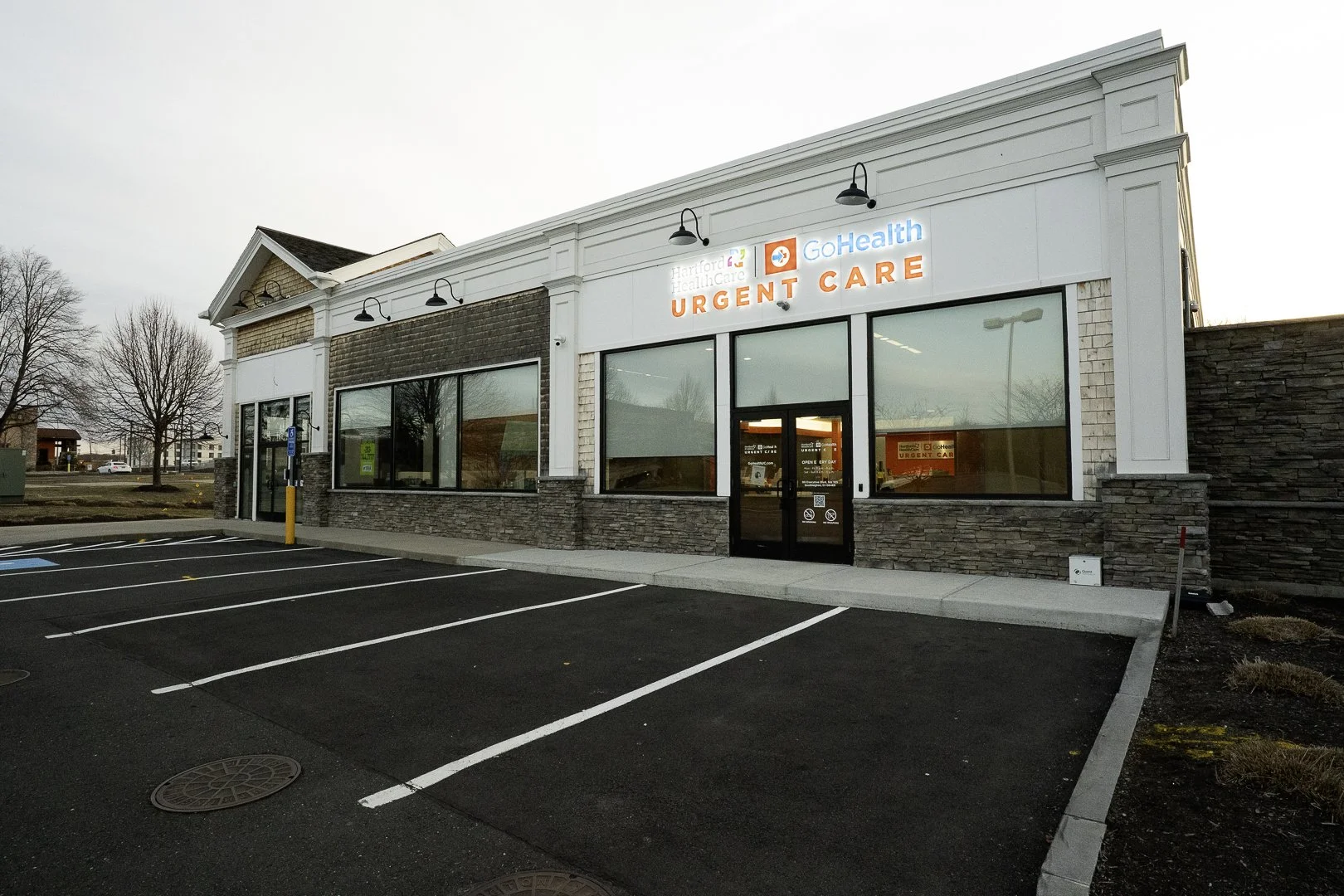 Exterior view of a medical urgent care center with parking lot in front, sign displaying Hartford Healthcare GoHealth Urgent Care.