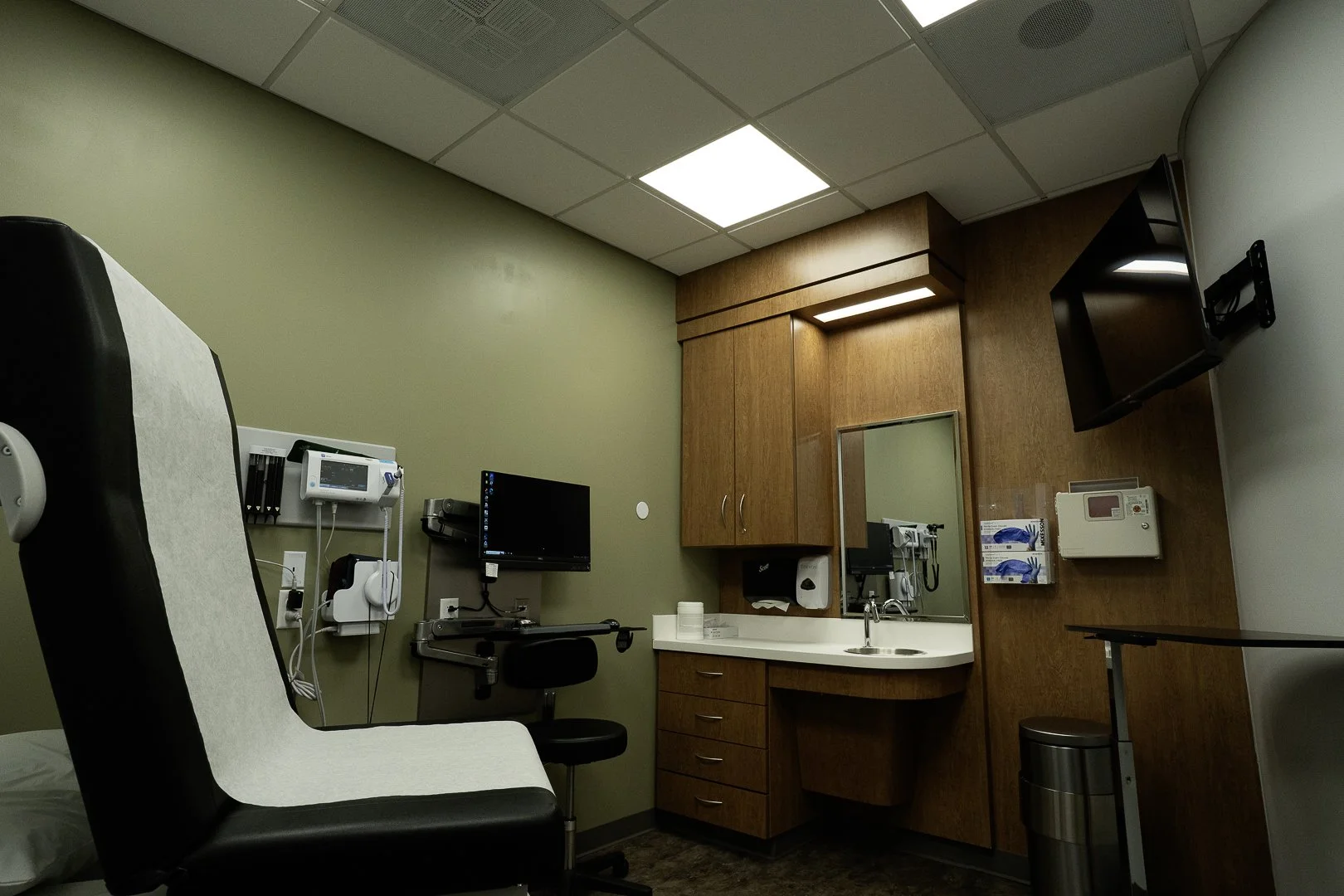 Medical examination room with a partitioned wall, green wall, medical equipment, and a patient chair.