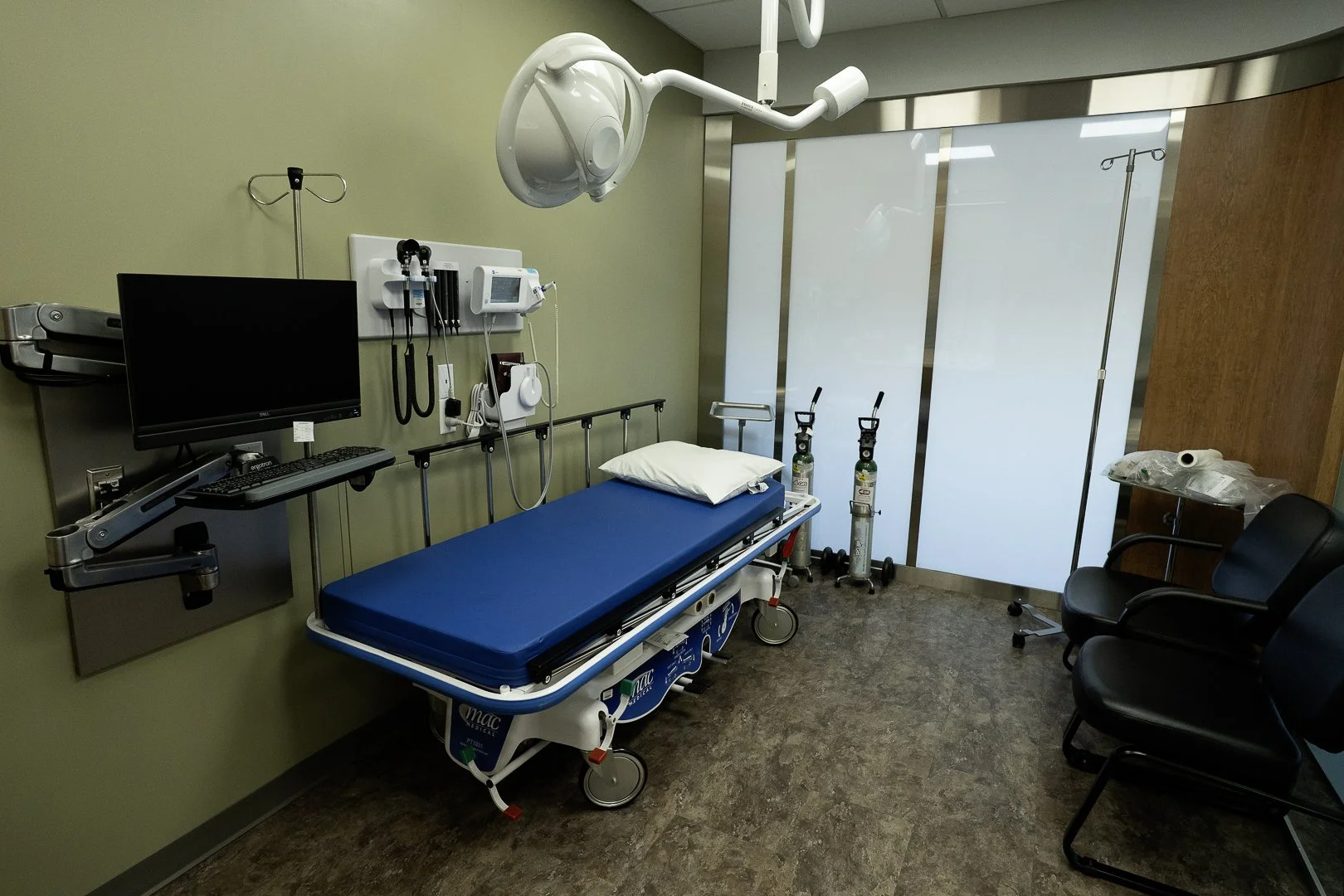 Hospital emergency room with a blue hospital bed, medical equipment, monitors, and IV stands, in a clean, sterile environment.