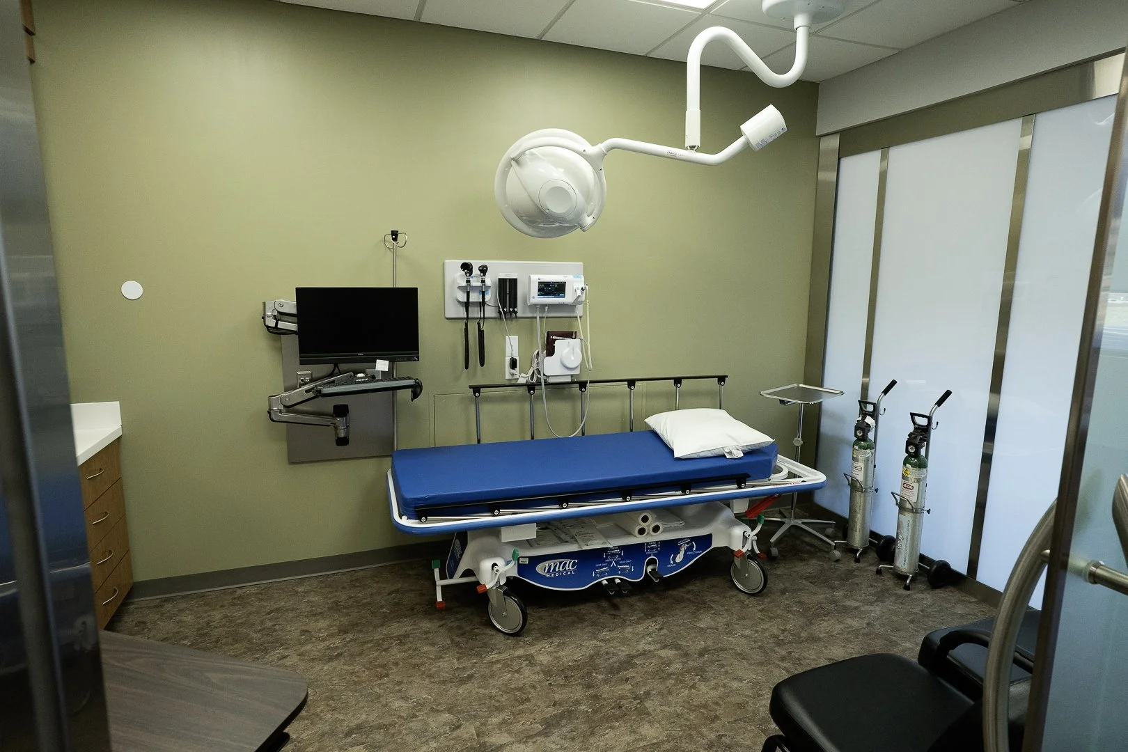 A hospital emergency room room with a hospital bed, medical equipment, and oxygen tanks.