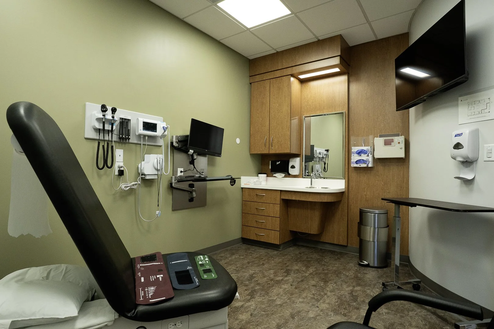 Empty examination room in a clinic with medical equipment, a doctor's chair, and a bed with pillow.