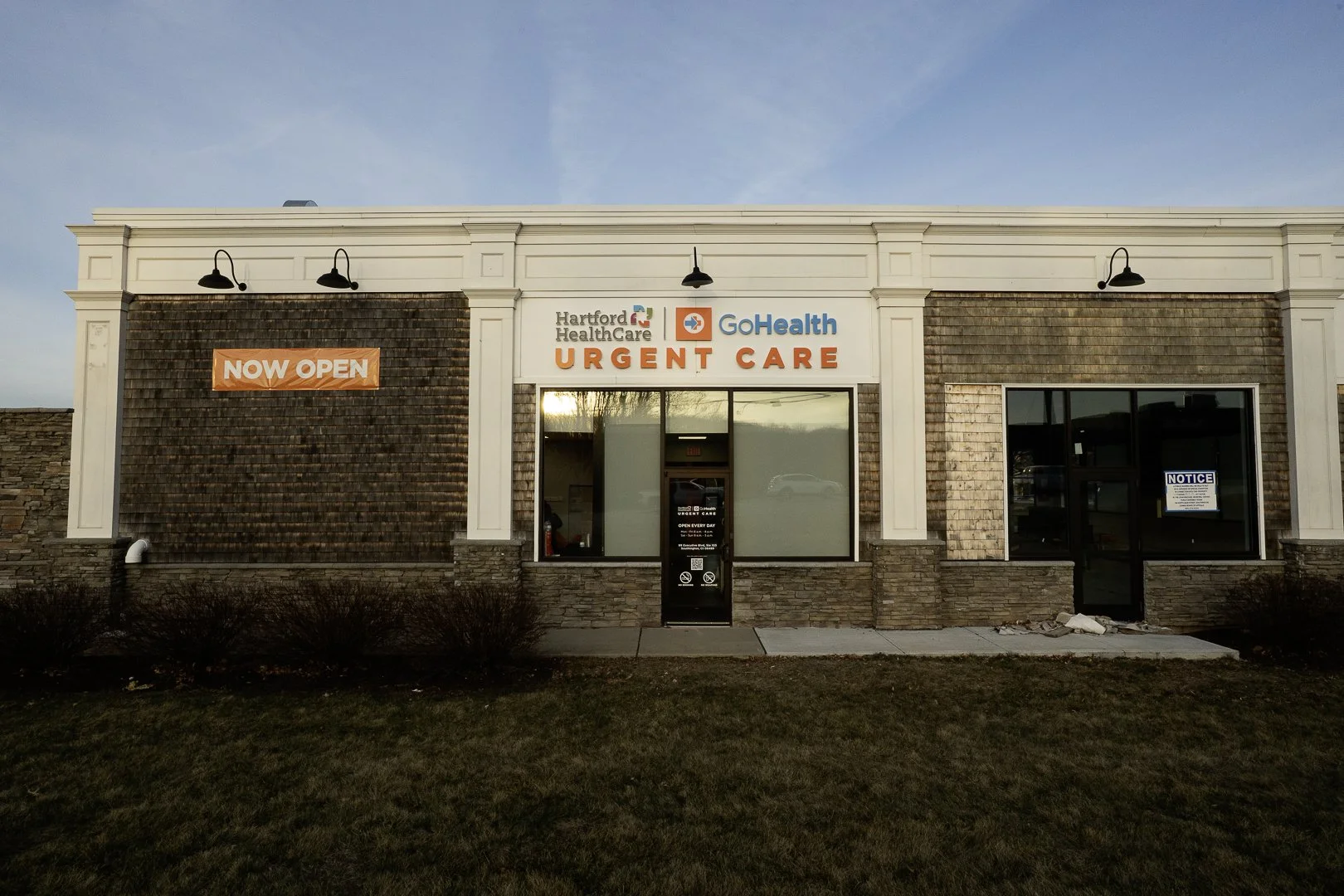 Exterior of Hartford Healthcare GoHealth Urgent Care building with a sign saying 'Now Open' and a large window and door at the front.