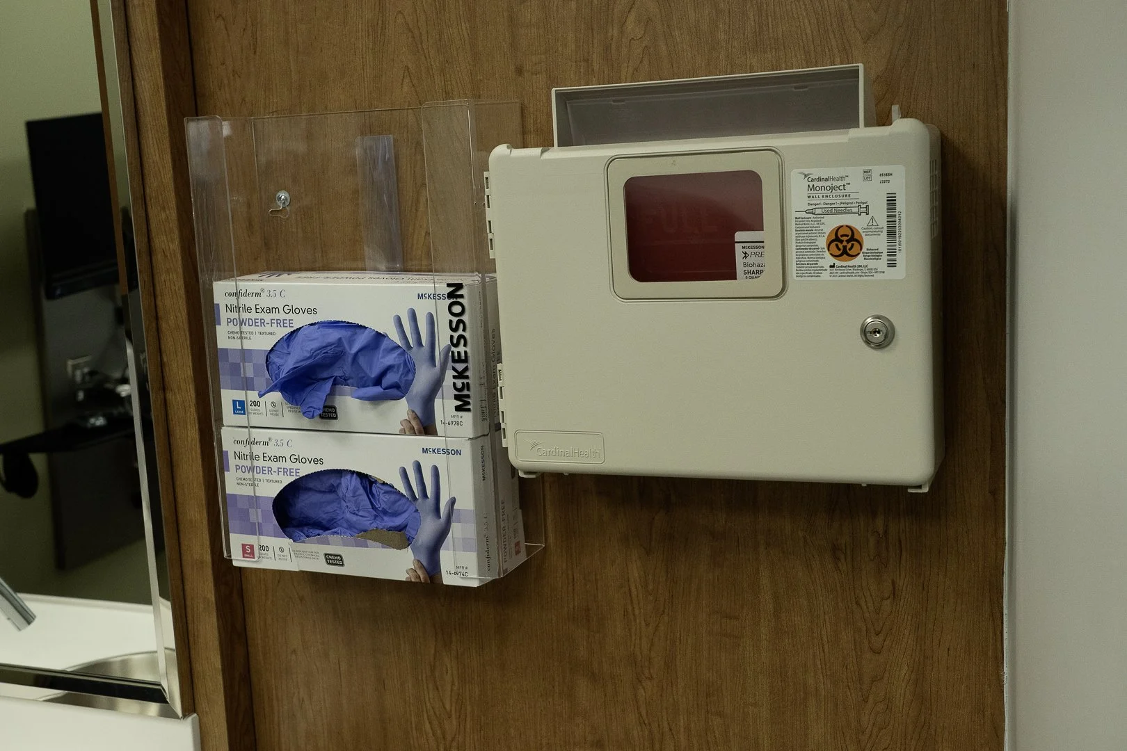 Box of blue nitrile exam gloves and a medical biohazard sharps container on a wooden door.