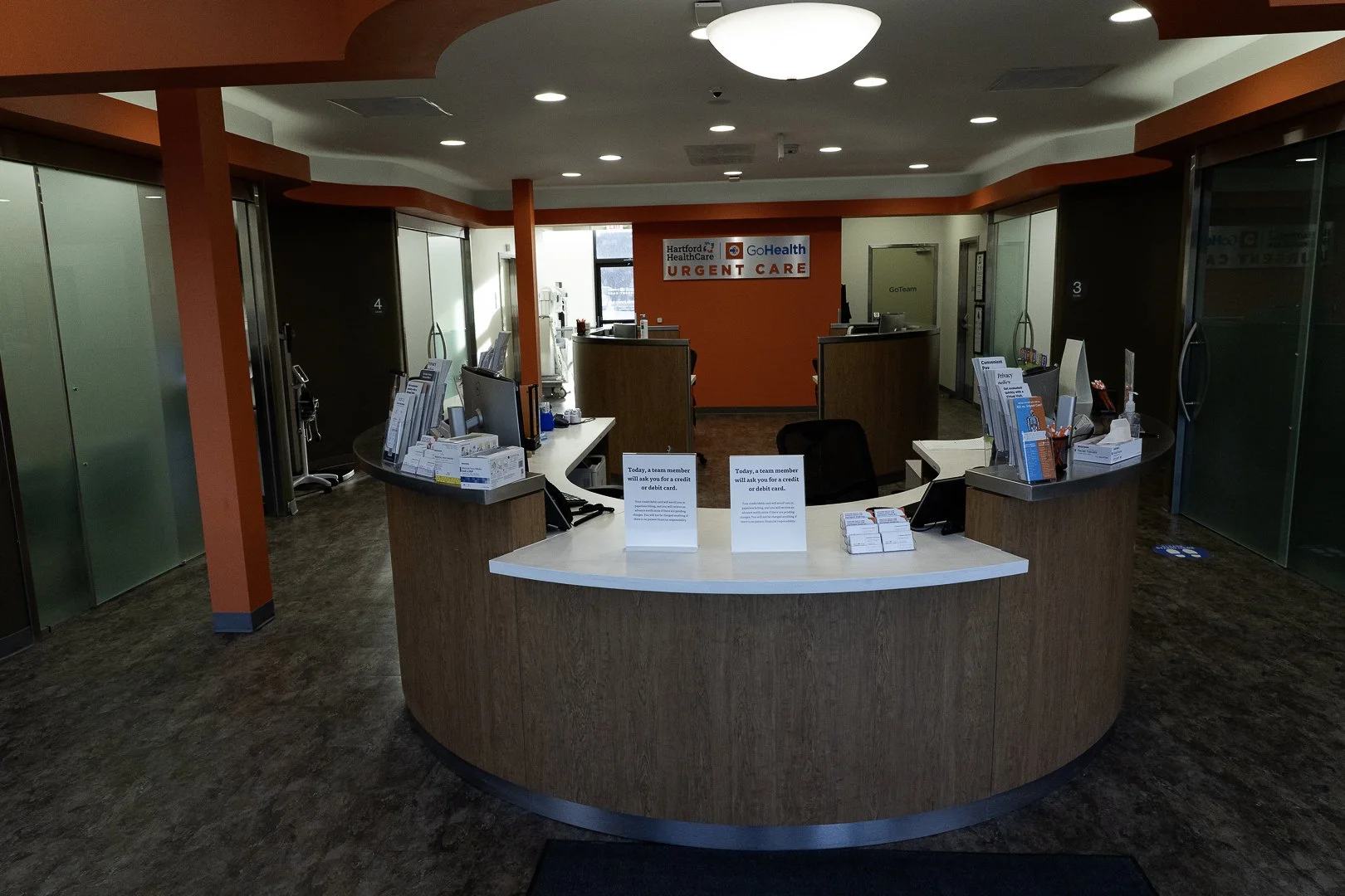 Reception area of Hartford HealthCare GoHealth Urgent Care with a curved front desk, informational signs, and a background wall with signage.
