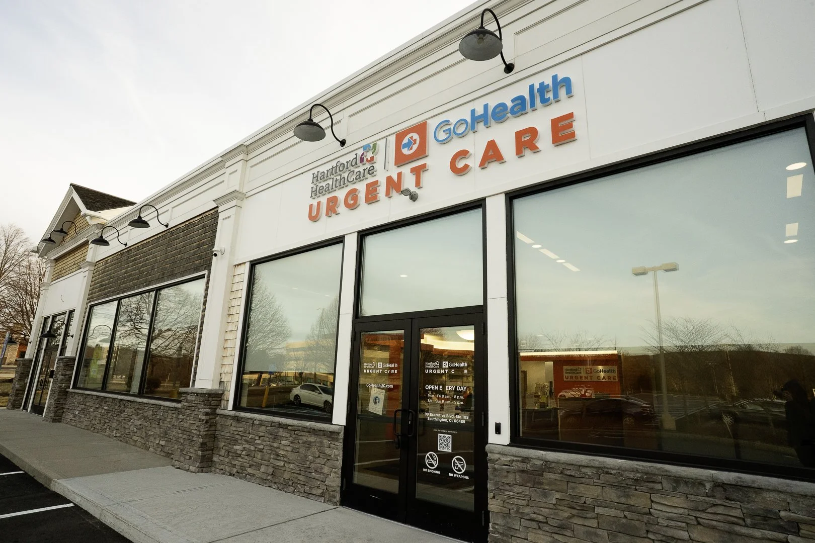 Exterior of a Hartford HealthCare Urgent Care clinic building with large windows, stone and siding facade, and signage including 'GoHealth' and 'Hartford HealthCare'