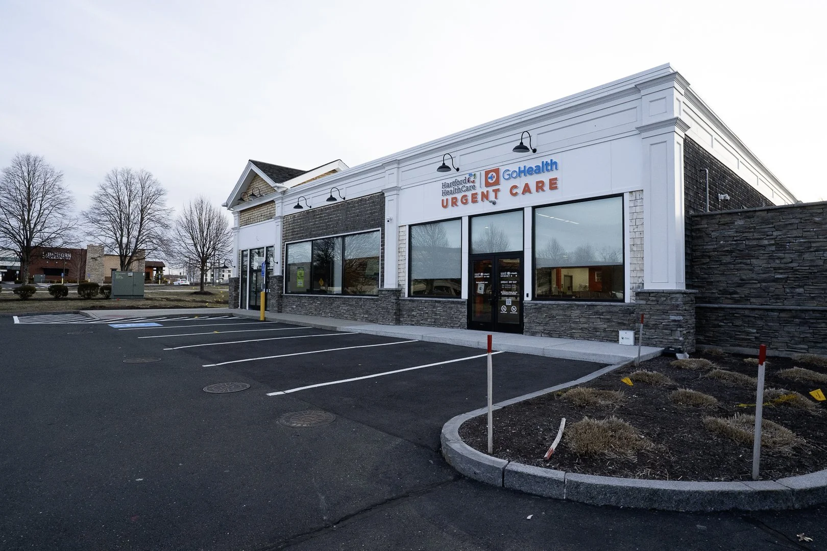 Exterior of GoHealth Urgent Care clinic with empty parking lot and leafless trees in background.