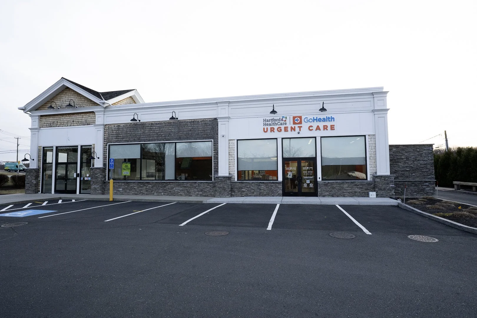 Exterior of a Hartford HealthCare Urgent Care building with large parking lot in front, clear sky, and no people visible.