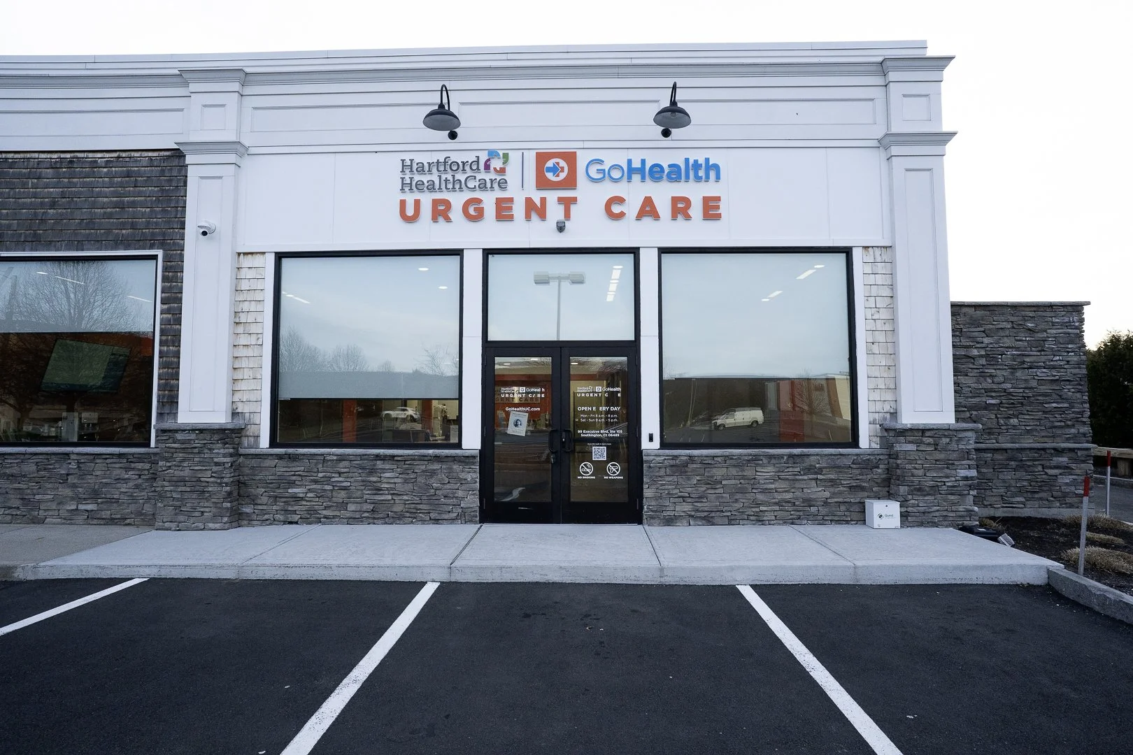 Front of a medical clinic with signage that reads 'Hartford HealthCare', 'GoHealth', and 'Urgent Care,' with parking spaces in the foreground.