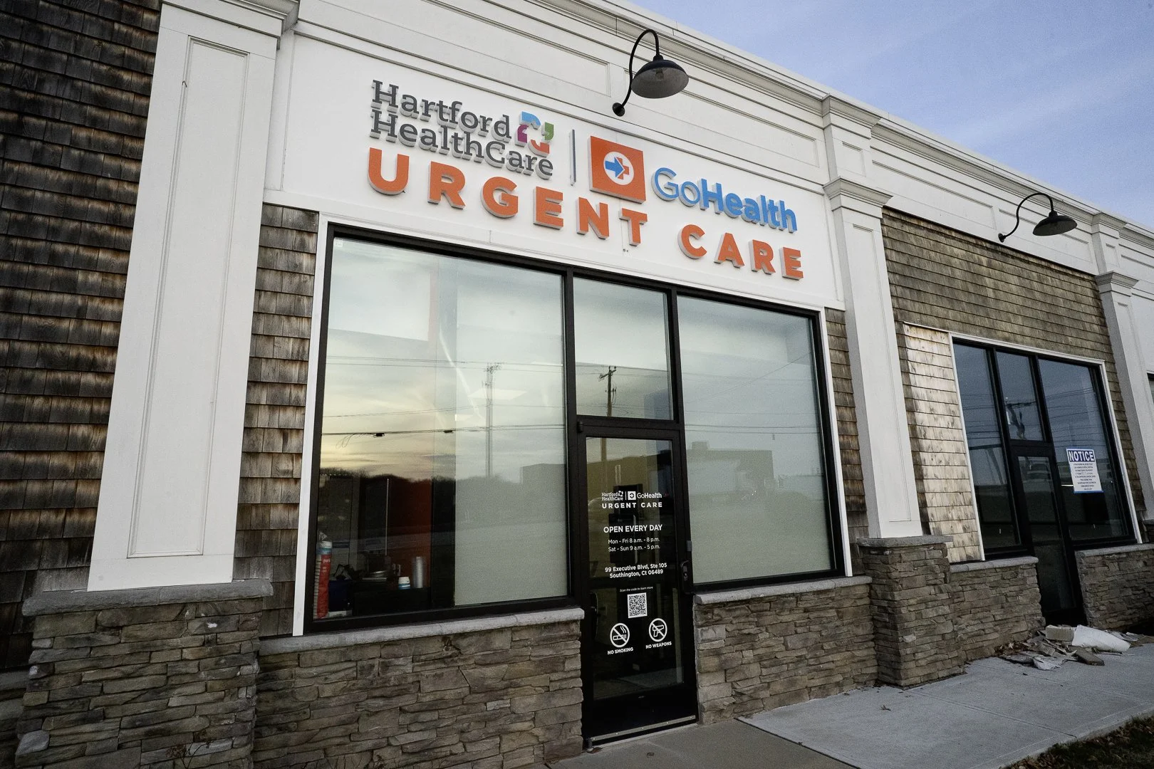Exterior of a healthcare urgent care facility with signs displaying Hartford Healthcare and GoHealth, front entrance with glass doors, and sidewalk