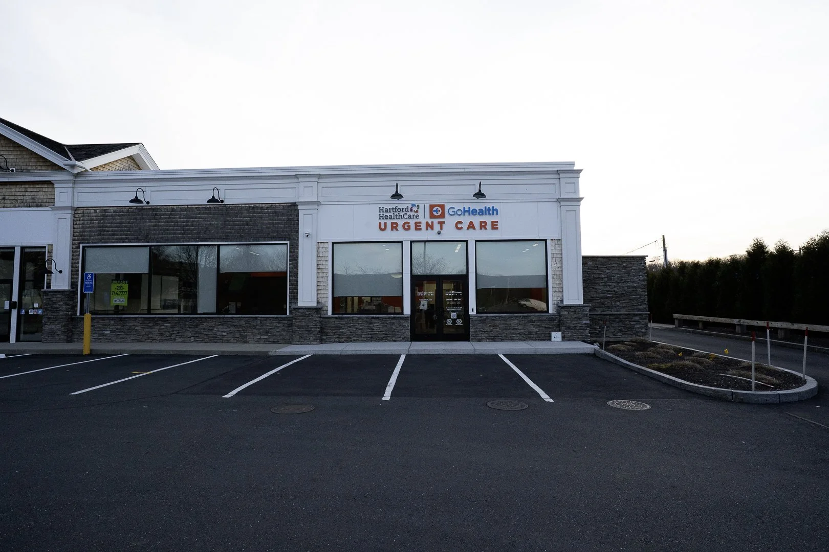 Exterior of a Hartford HealthCare Urgent Care building with parking lot in front, large windows, and a sign displaying healthcare providers' names.