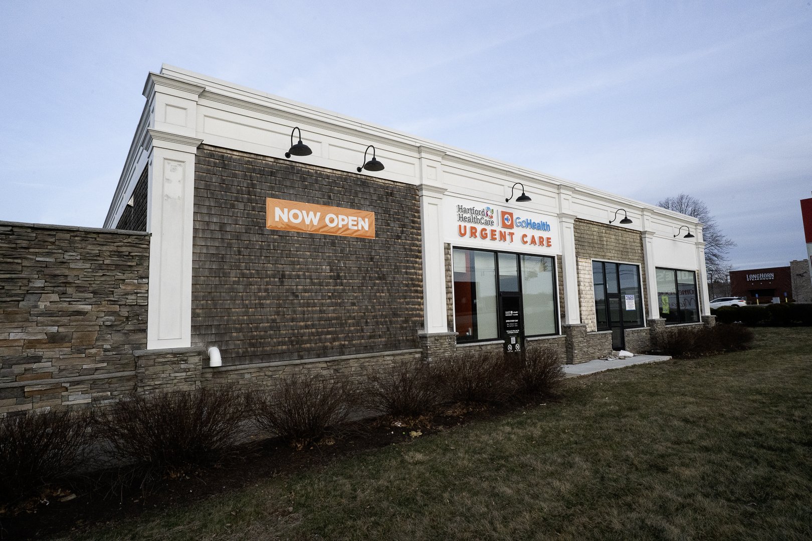 Exterior of a healthcare building with signs indicating it is now open and offers urgent care services.