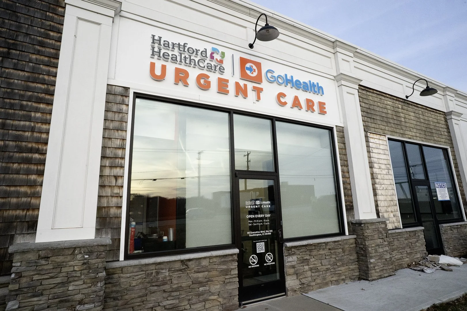 Exterior of a healthcare clinic with signs for Hartford Healthcare, GoHealth, and Urgent Care, featuring large windows and a door.