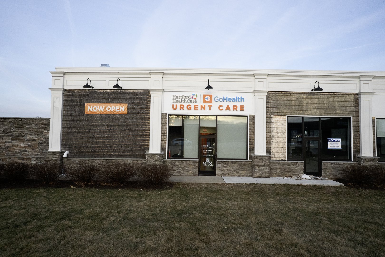 Front view of a commercial building with signs for Hartford HealthCare GoHealth Urgent Care, indicating it is now open.