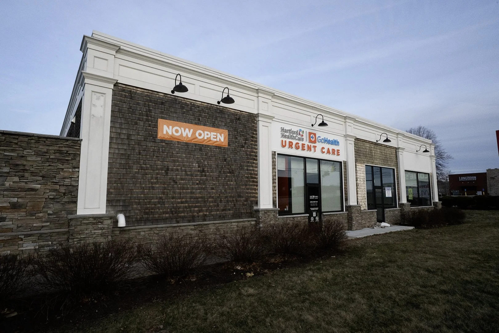 Exterior of an urgent care building with a sign that reads 'NOW OPEN' and a sign indicating it is part of Hartford HealthCare and GoHealth Urgent Care.