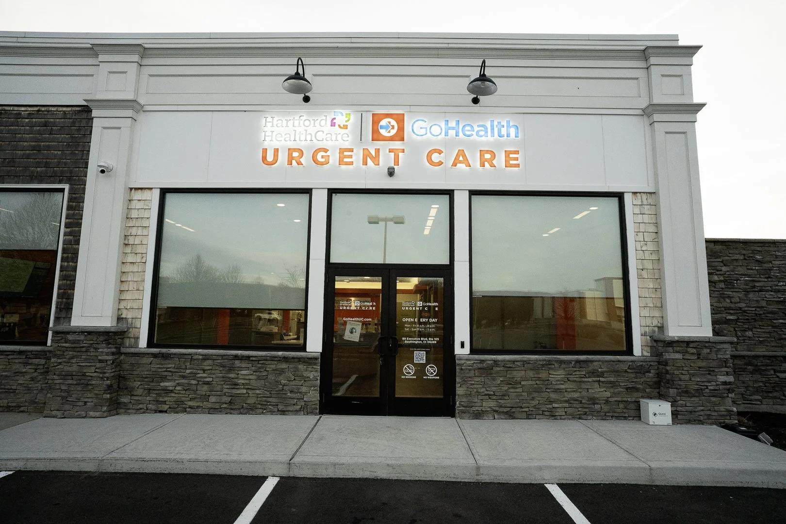 Exterior of an urgent care medical facility with signs for Hartford Healthcare and GoHealth, large windows, and parking spaces in front.