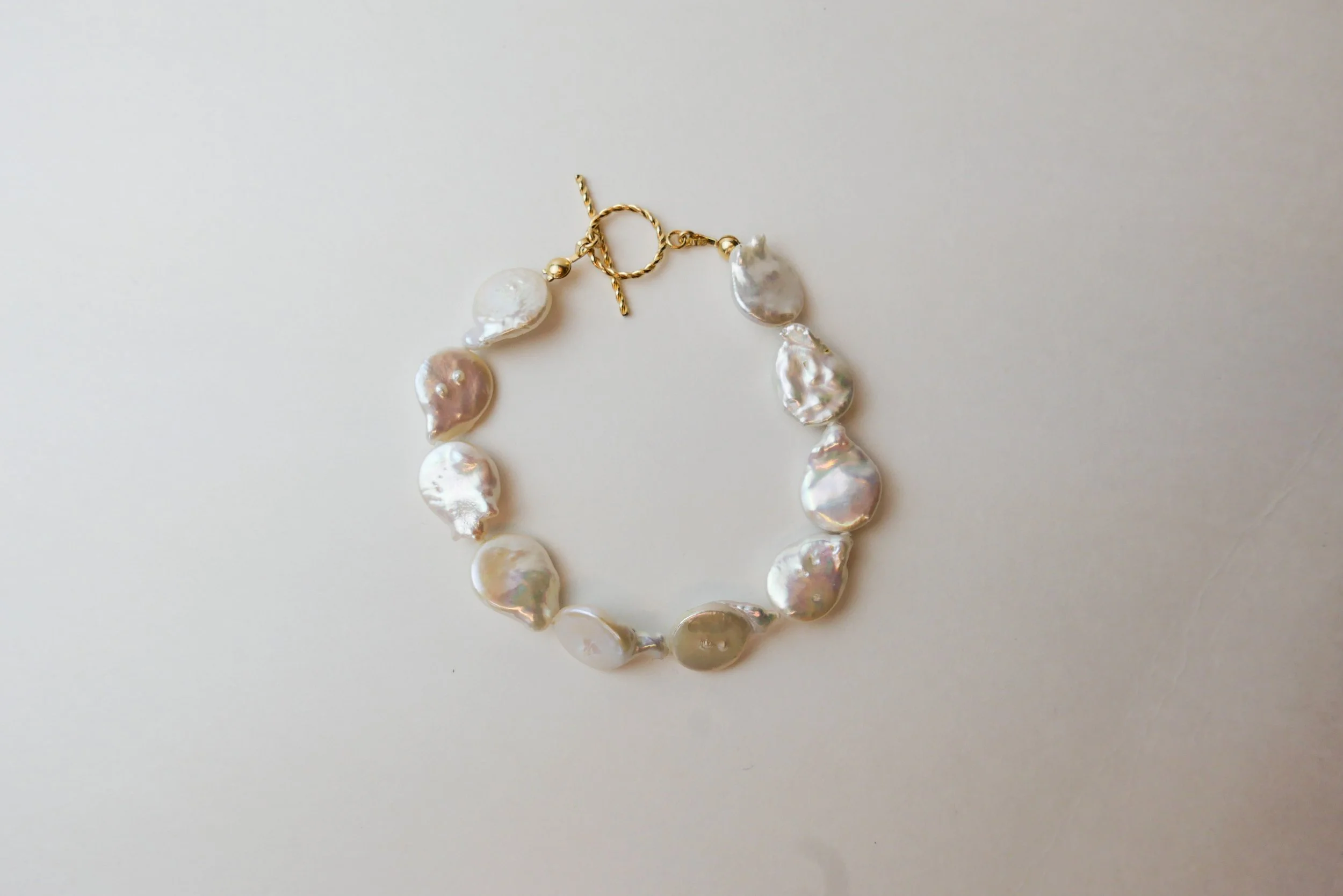 A necklace made of large, irregularly shaped white pearls with a gold clasp and chain, laid out on a white surface.