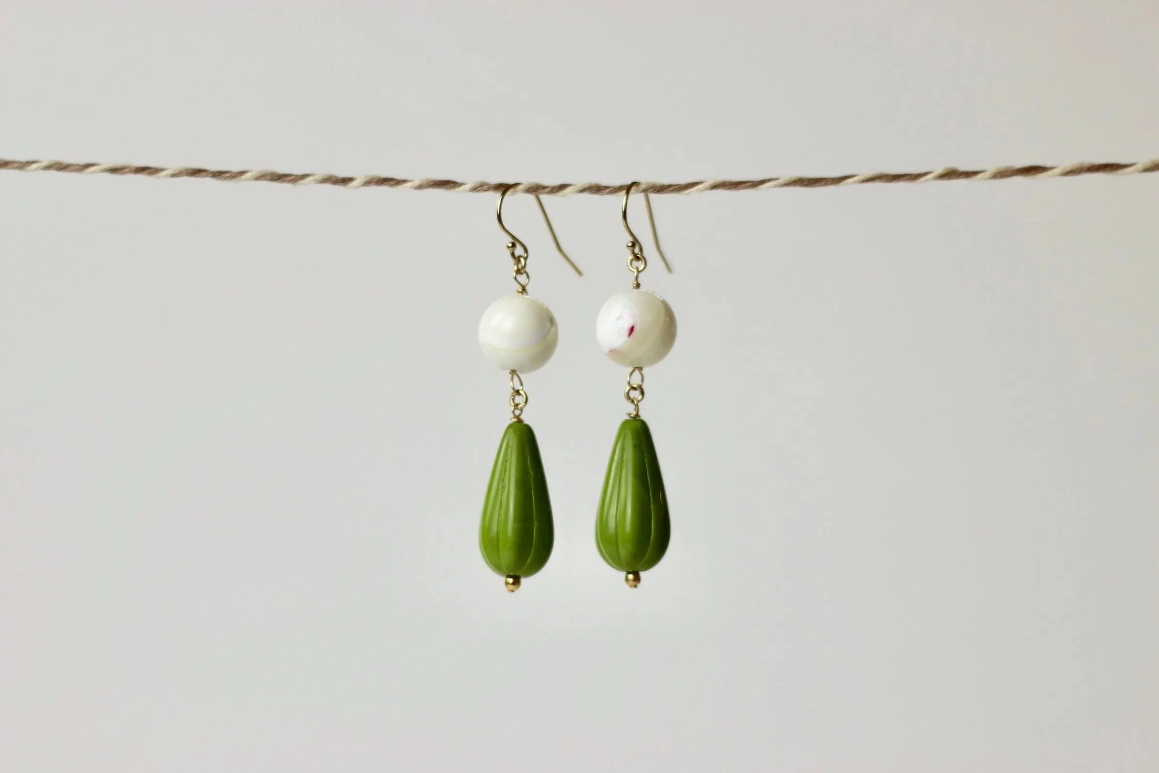 Pair of earrings hanging from a thin string, with white and green beads against a plain white background.
