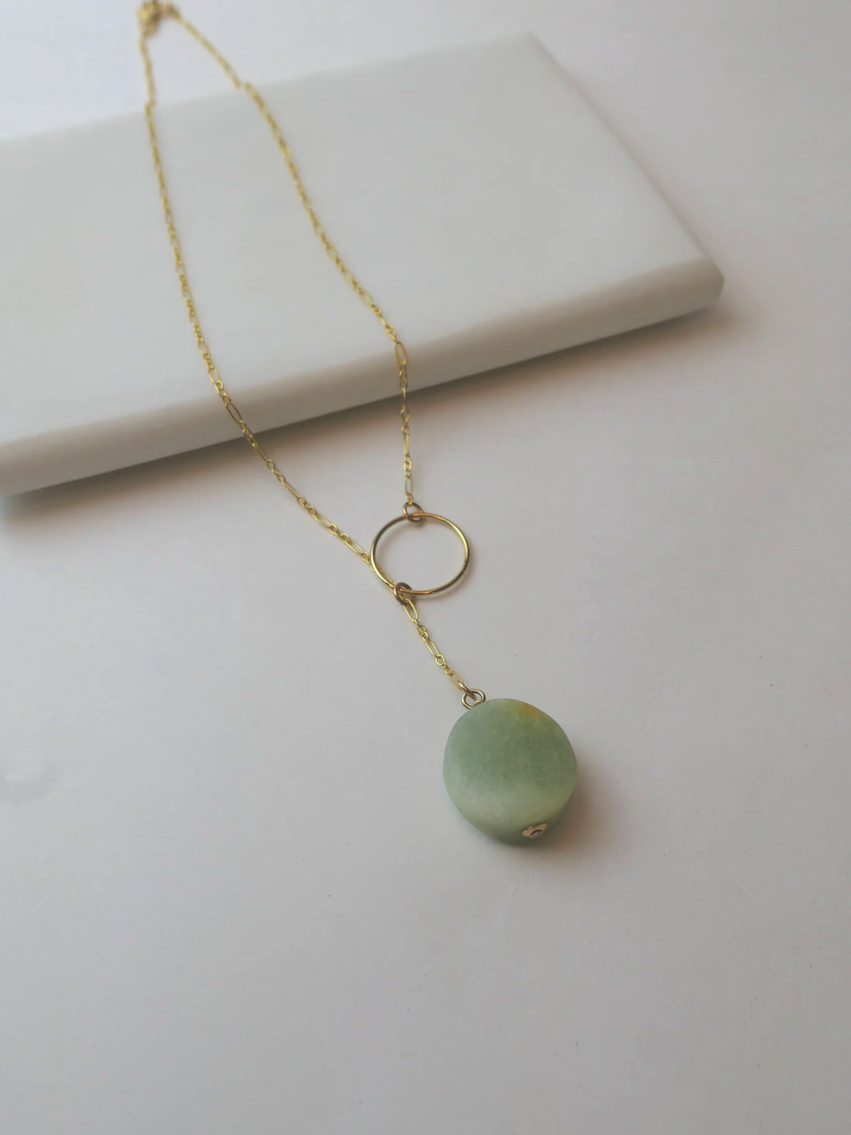 Gold necklace with a round green pendant resting on a white box and surface.