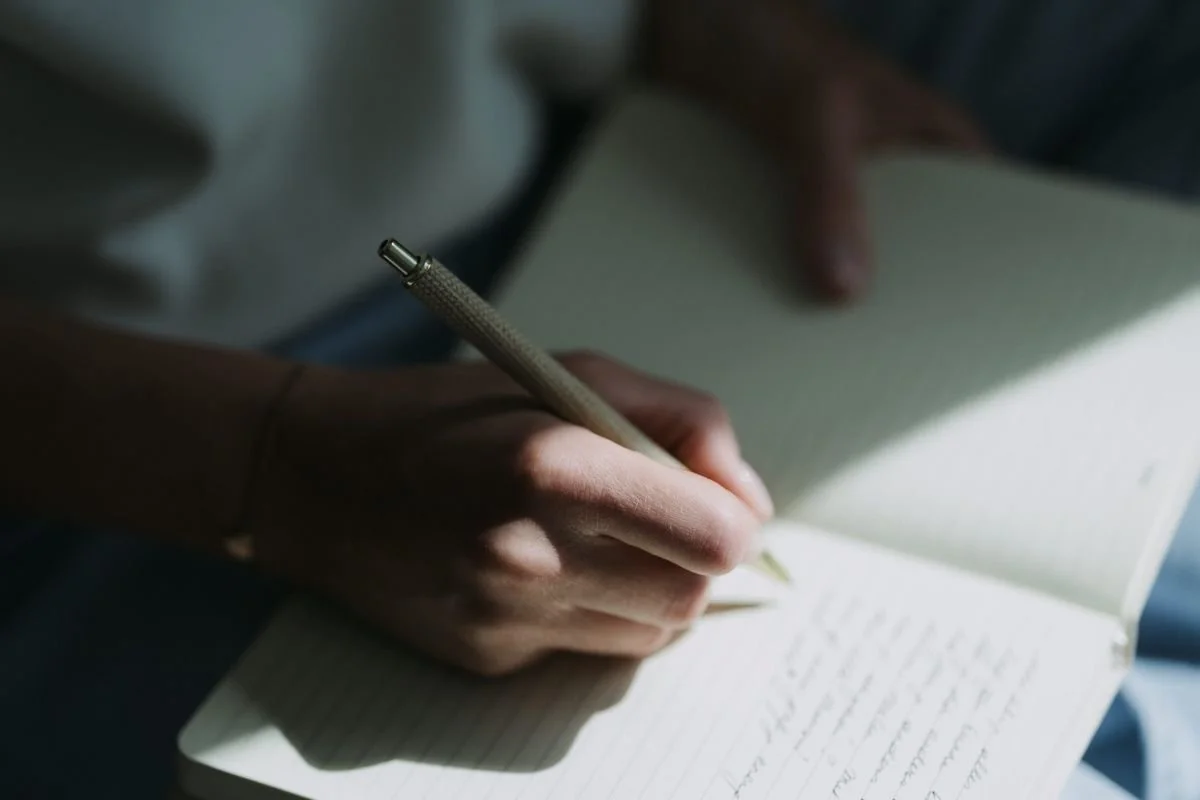 Een hand die schrijft in een notitieboekje met een pen.