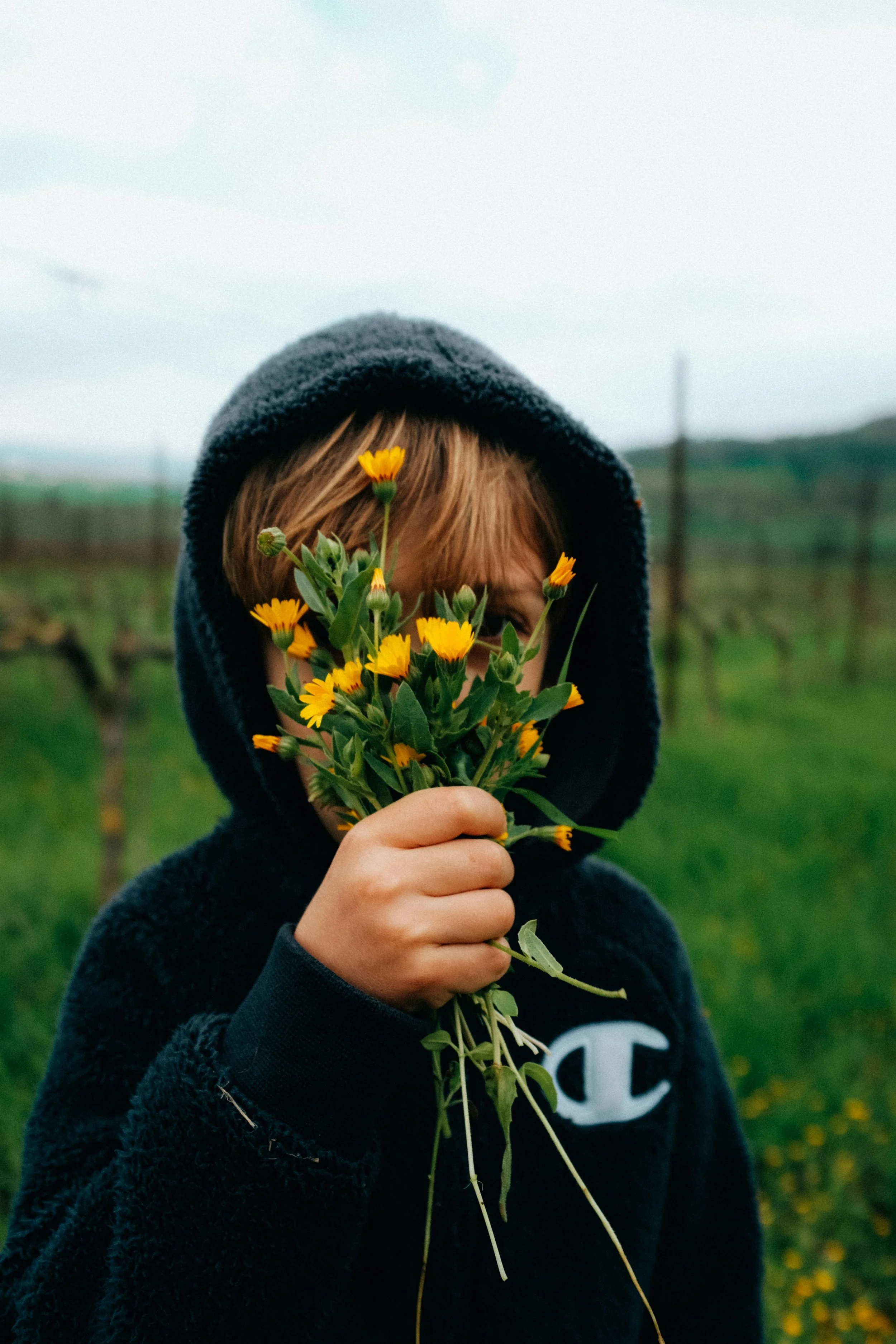 A child holding a bunch of yellow flowers in front of their face outdoors.