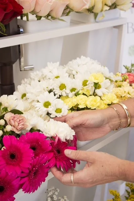 Person selecting pink flowers from a display of various colorful flowers in a store.