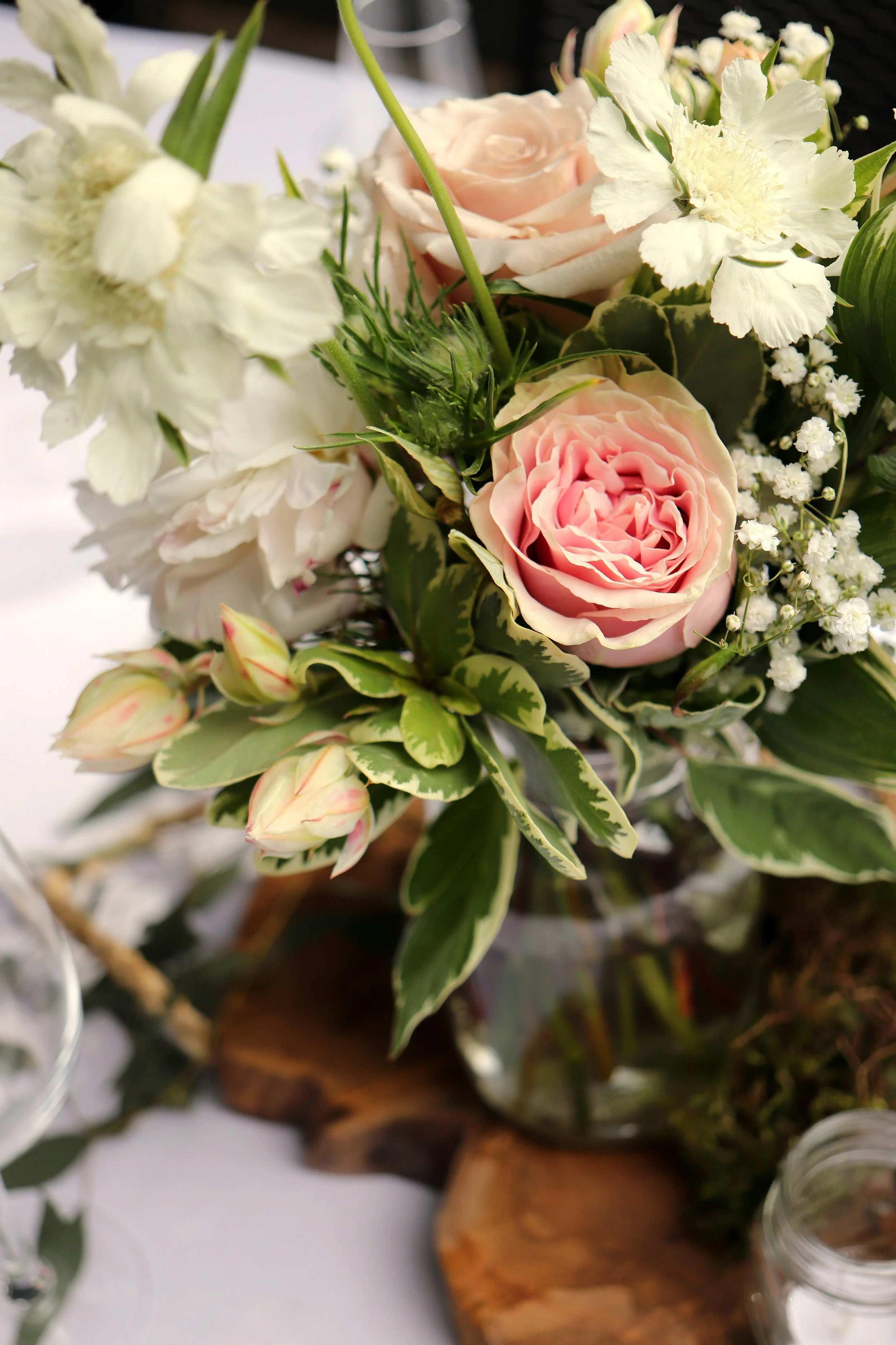 Close-up of a floral arrangement with pink roses, white carnations, and baby's breath, on a wooden base with a white background.