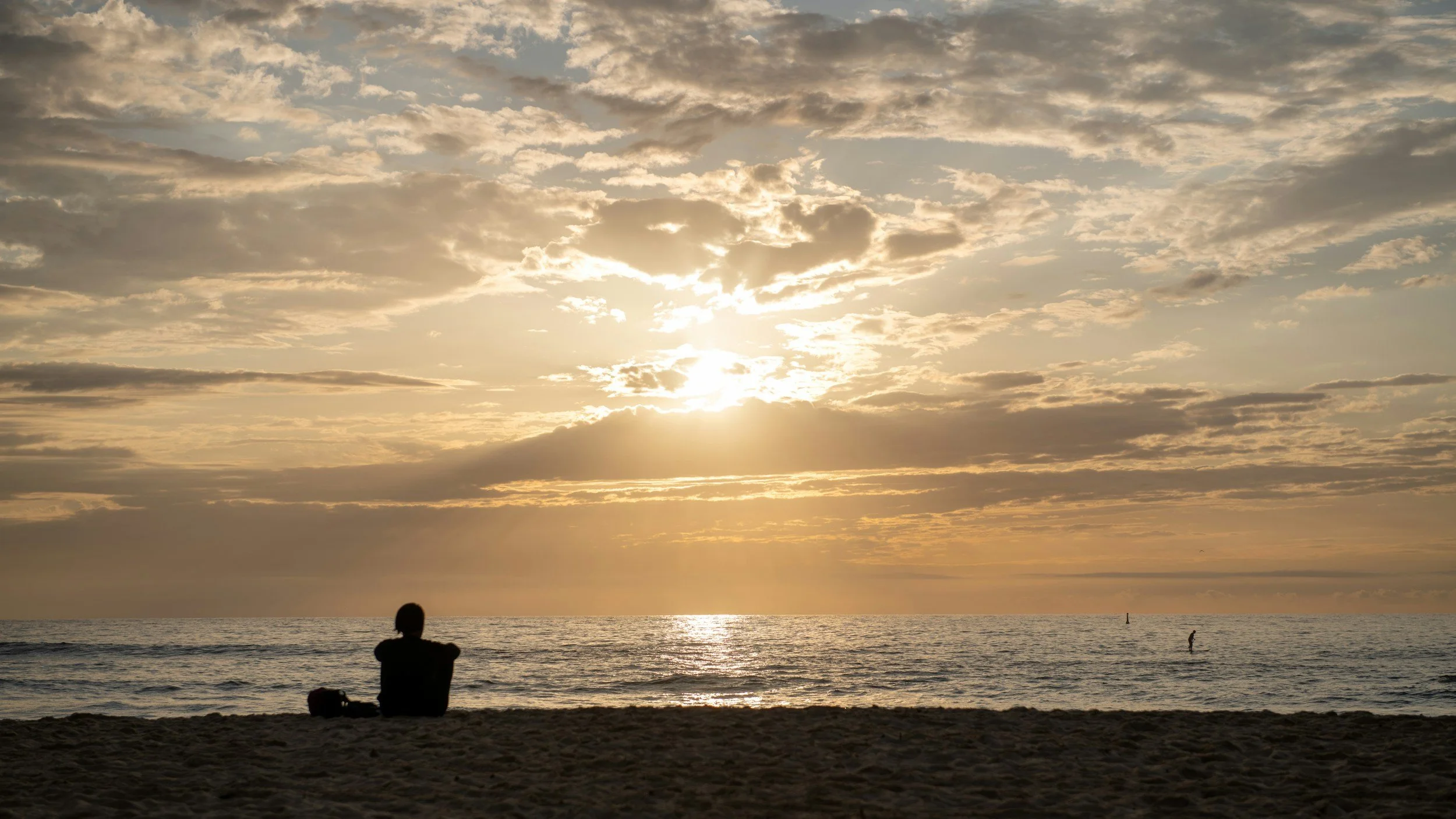 A woman is sitting in a chair looking out at the ocean, symbolizing the feelings of calm, clarity and wellness clients can find in therapy.