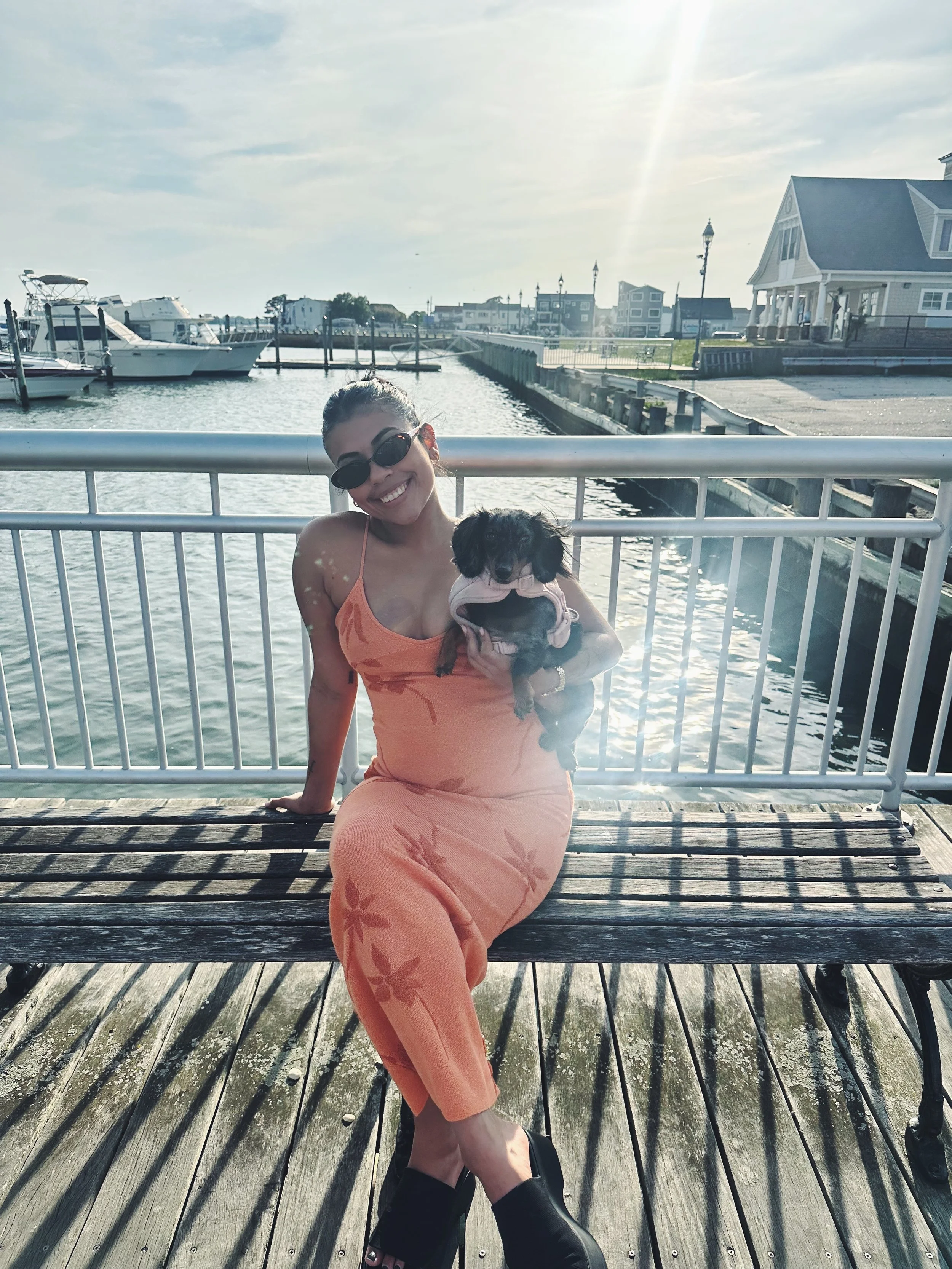 Therapist for high achieving woman sitting on a wooden dock, smiling, holding a small black dog.