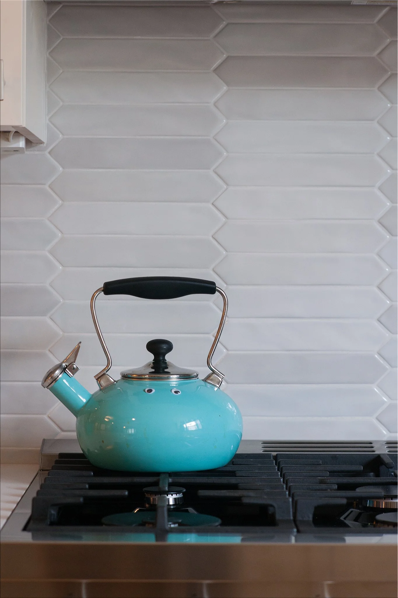 A teal kettle with googly eyes on a stovetop in a kitchen.