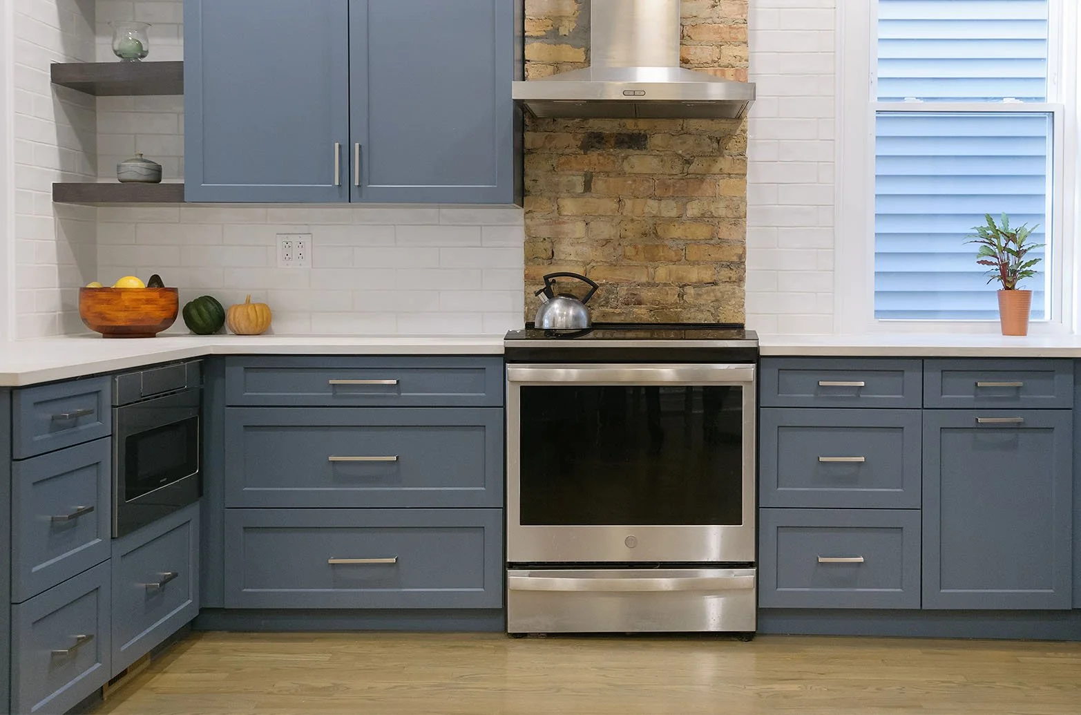 Modern kitchen with blue and white cabinets, marble countertops, stainless steel appliances, and a central island with a flower arrangement.