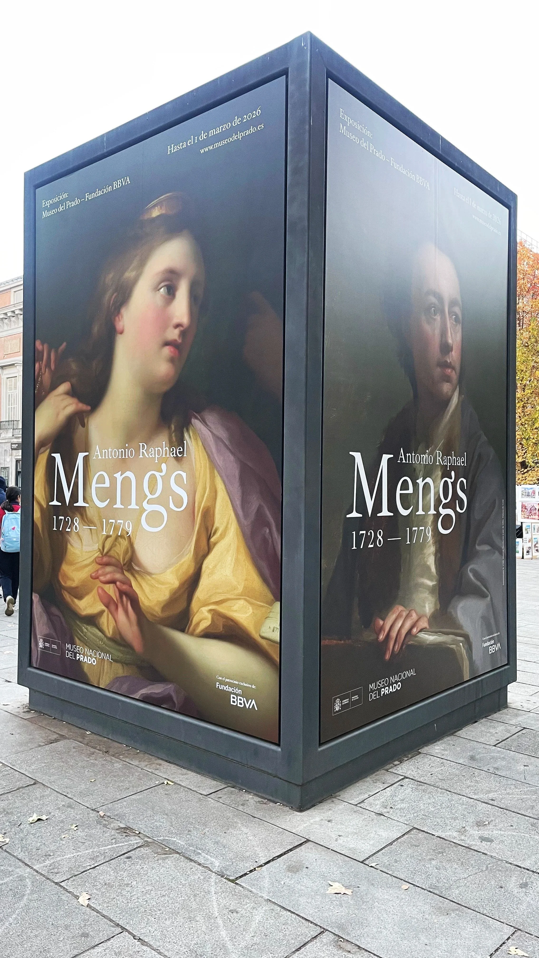 Advertisement for an art exhibition by Antonio Raphael Mengs at Museo del Prado, showing details of two classical paintings of a young woman and a young man, with text about the exhibition dates and museum location.