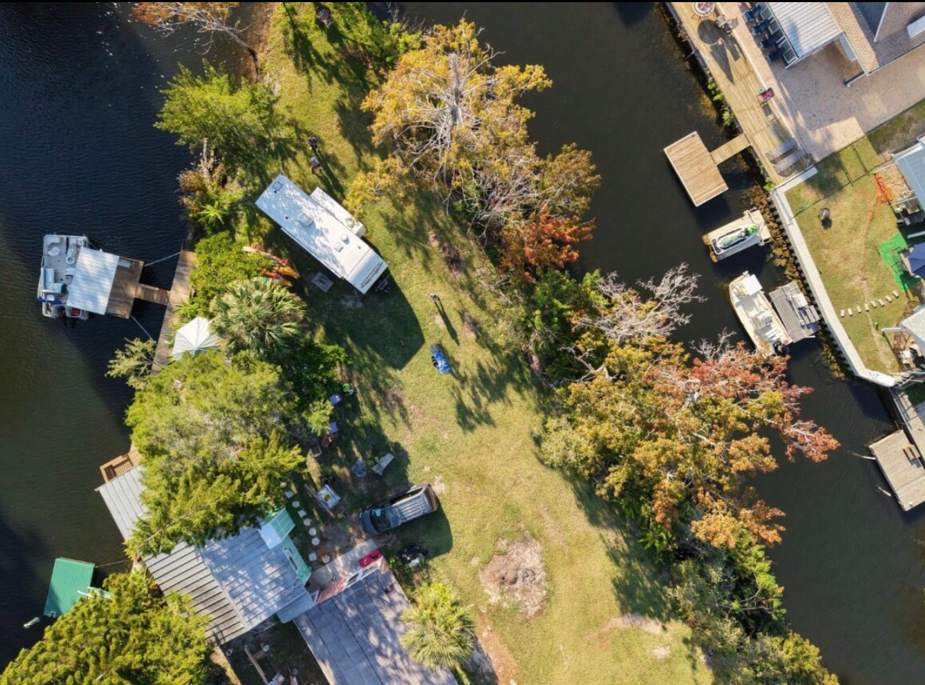 Aerial view of a riverside residential area with docks, boats, and trees with autumn foliage.