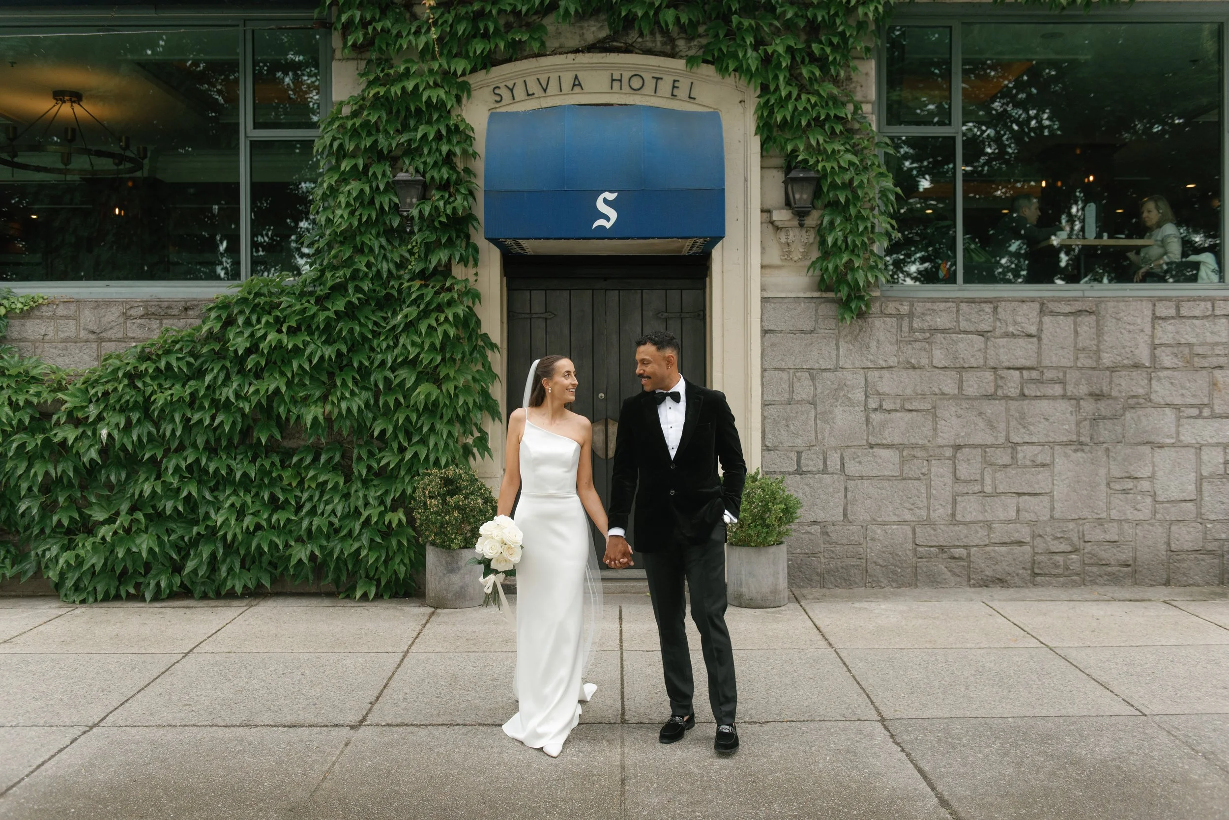 bride and groom holding hands on their wedding day with a white bouquet in downtown vancouver