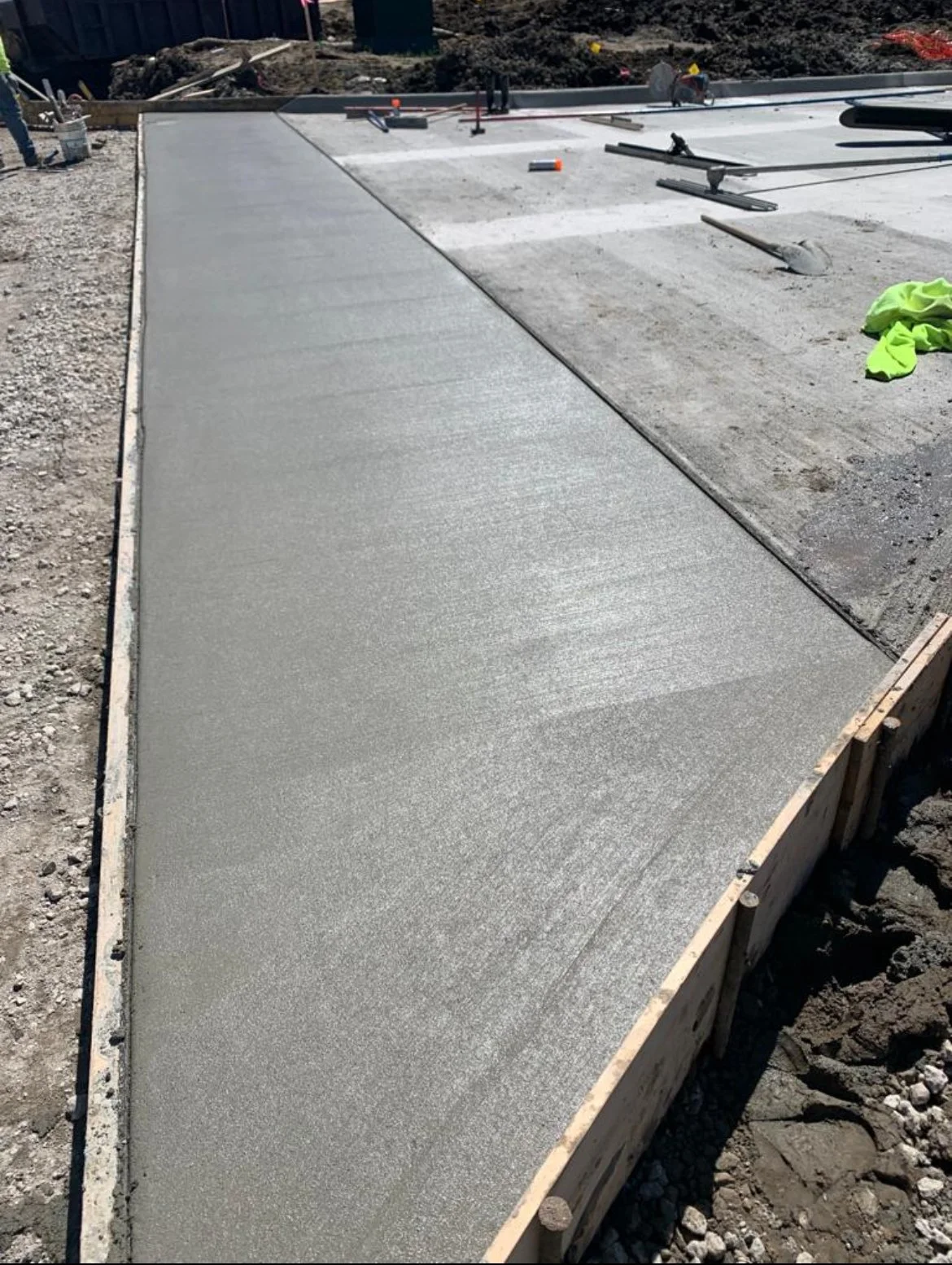 A freshly poured concrete slab on a construction site, with wooden and metal framework, construction tools, and supplies in the background.