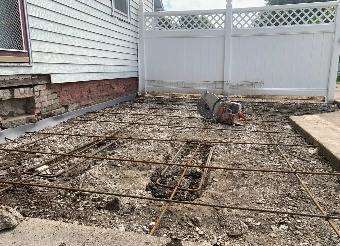 A residential construction site with exposed rebar on the ground for a concrete slab, with a concrete saw resting on the gravel.