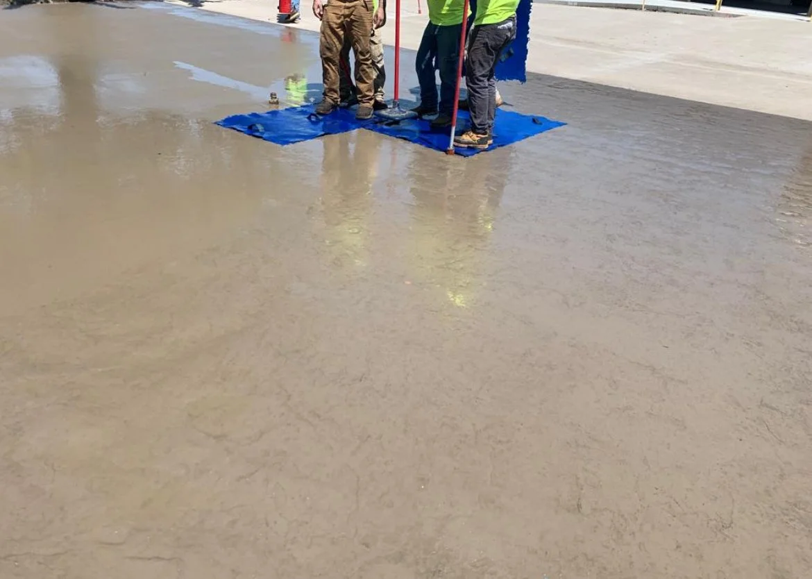 Construction workers standing on freshly poured concrete with a blue tarp underneath.