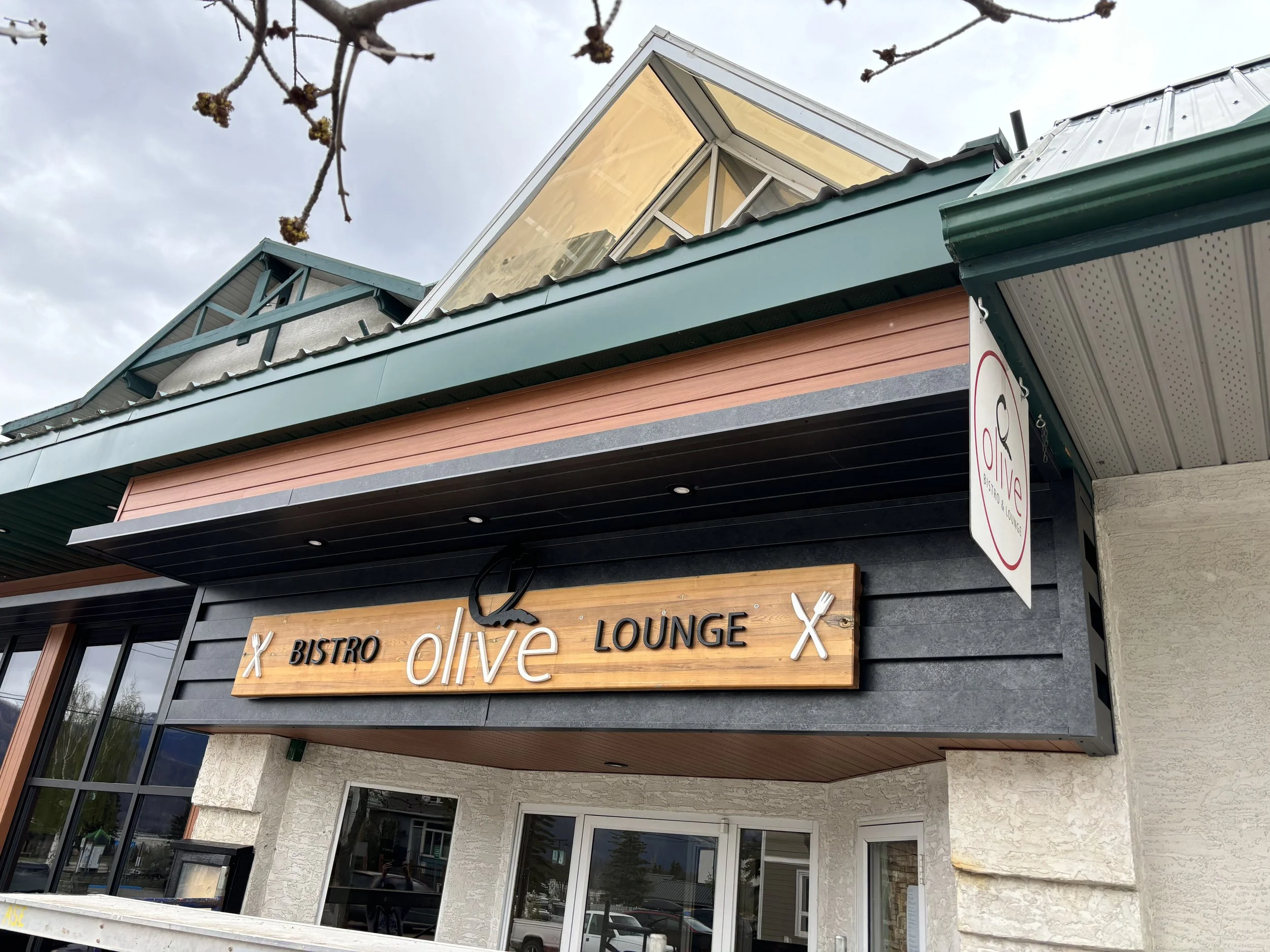 Exterior view of Olive Bistro and Lounge restaurant with a wooden sign and small windowed roof structure above.