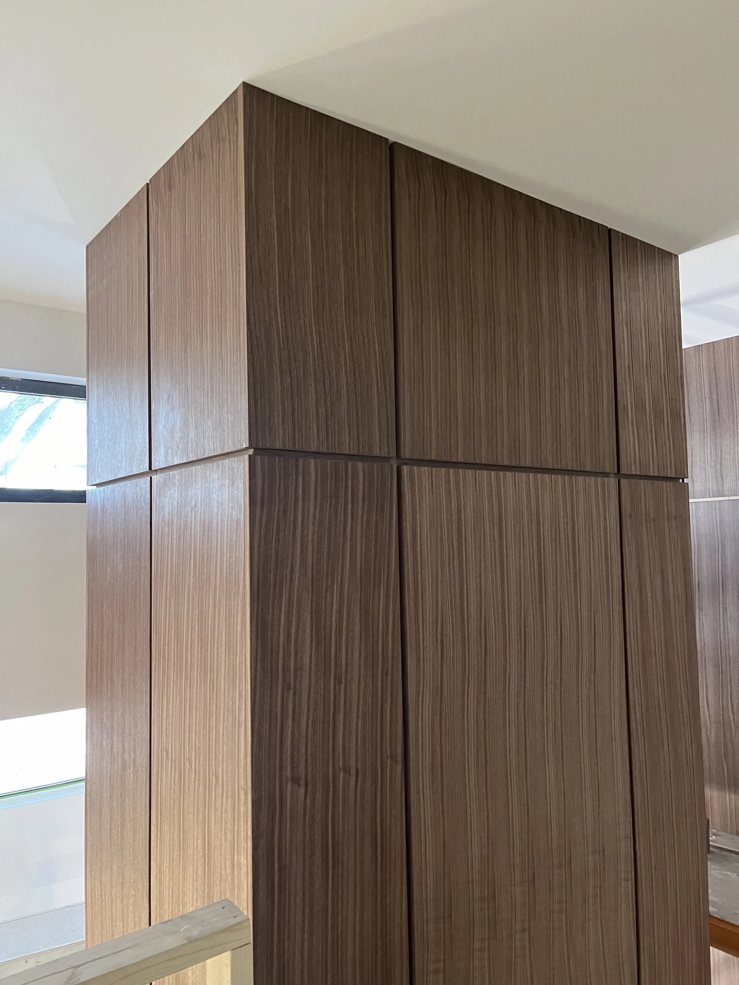 Close-up of a wooden corner construction with vertical grain, inside a modern building with windows and white ceiling.