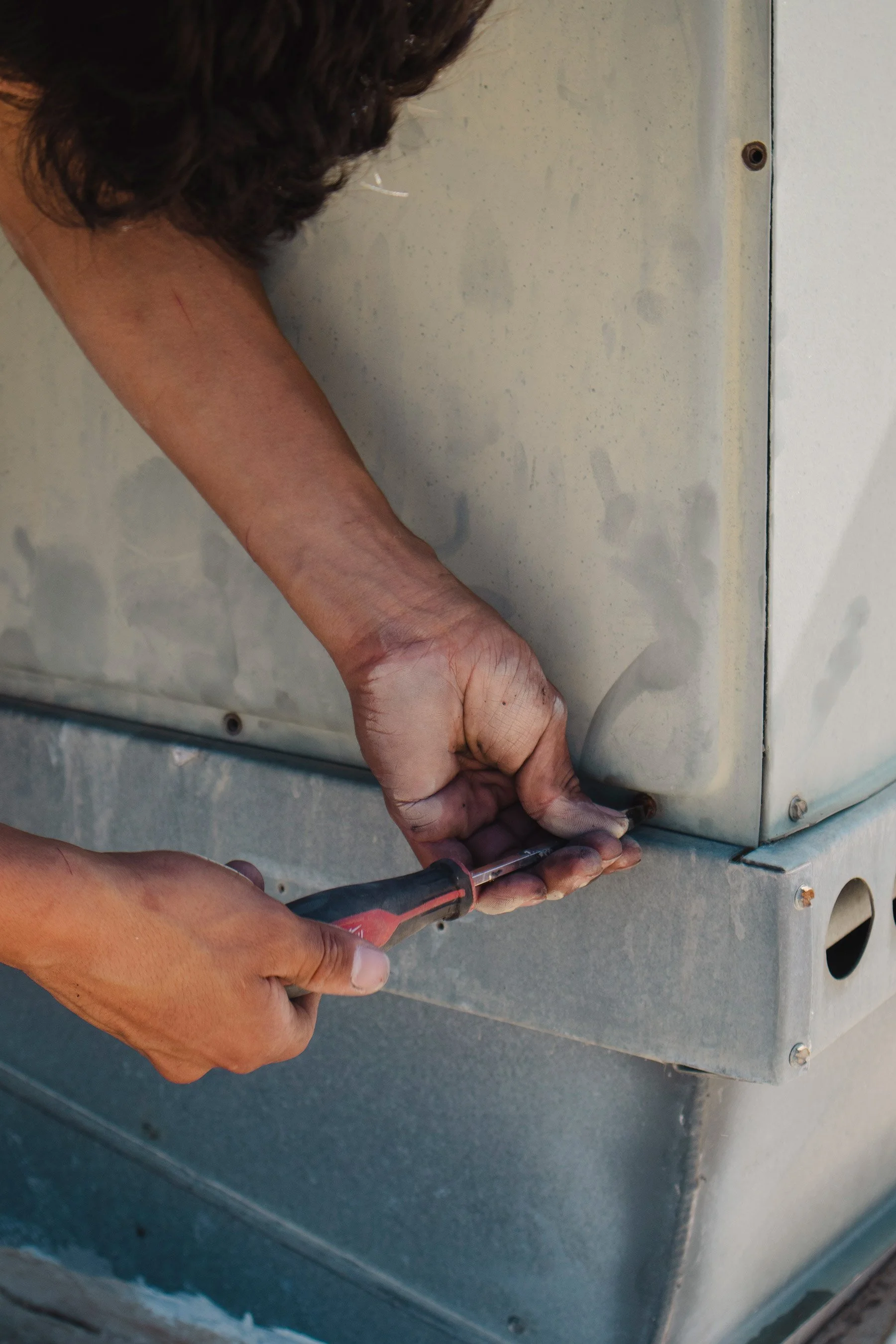 A person using a screwdriver to repair or work on an outdoor metal appliance or device.