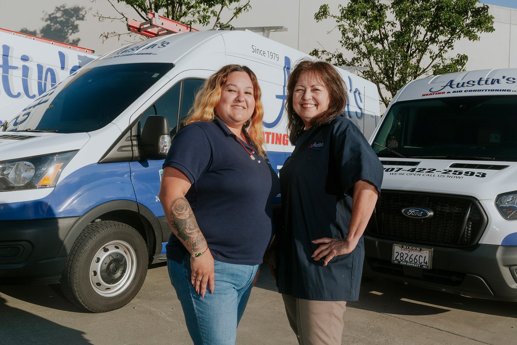 Two women standing in front of branded service vans for Austin's Heating & Air Conditioning, smiling at the camera.