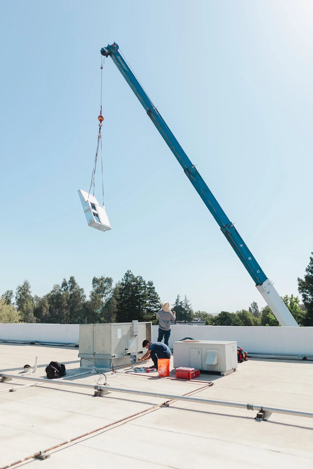 Construction workers on a rooftop operating a crane lifting a small house model.