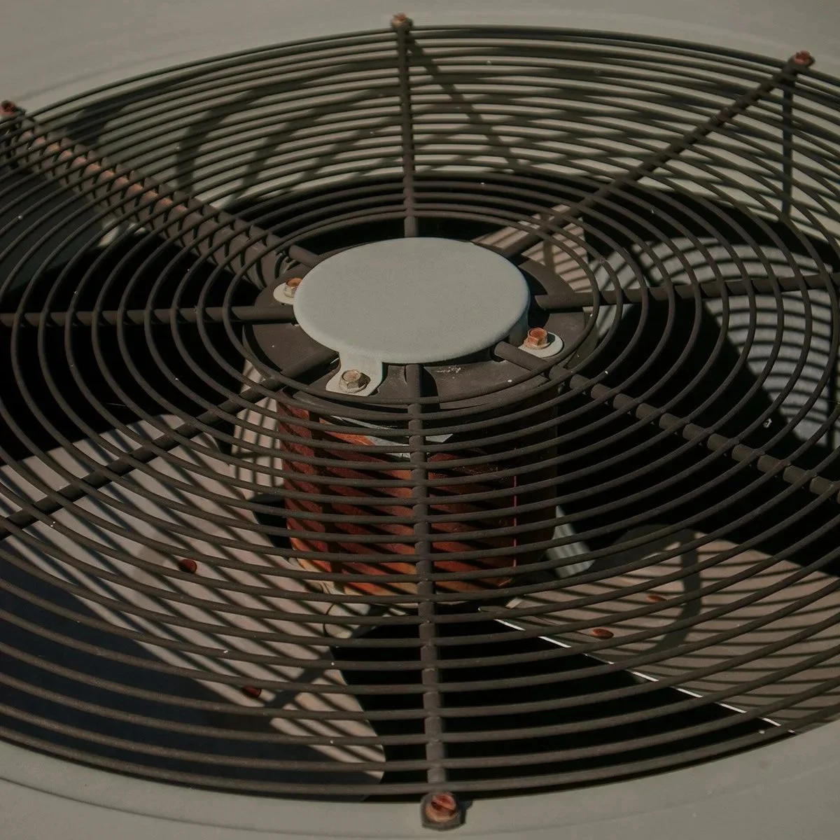 Close-up of a black fan grill with a white center circle, covering a fan or heater vent with visible screws and metal components.