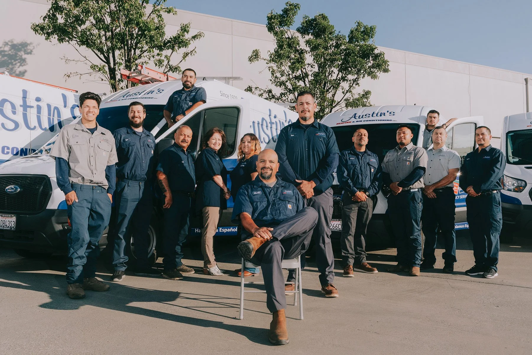 Group of people, including men and women, standing in front of company service trucks with the logo 'Austin's' on them. Some are smiling and posing for the photo outdoors on a sunny day.