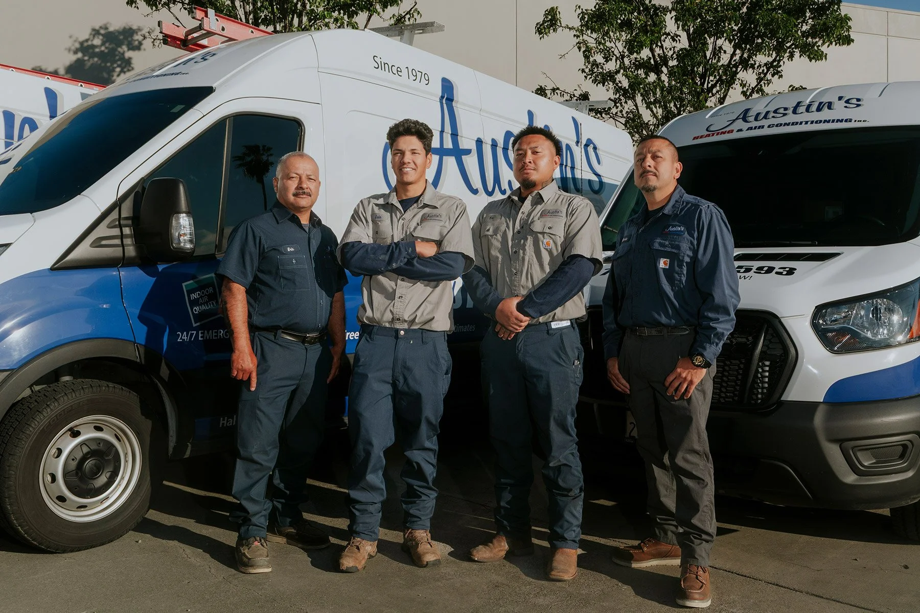 Four men standing in front of two trucks with Austin's branding, wearing work uniforms, outdoors on a sunny day.