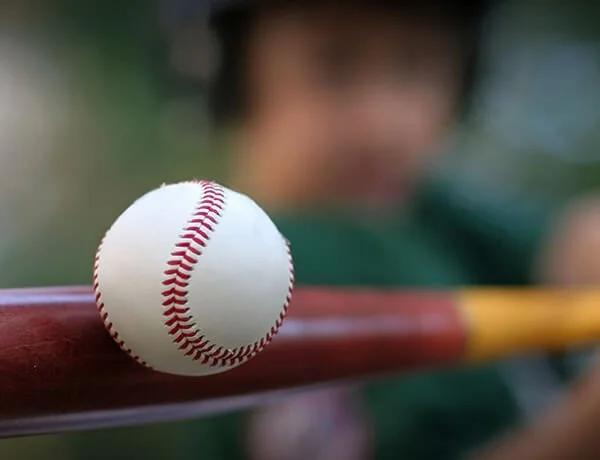Close-up of a baseball on a bat with a child's face blurry in the background.