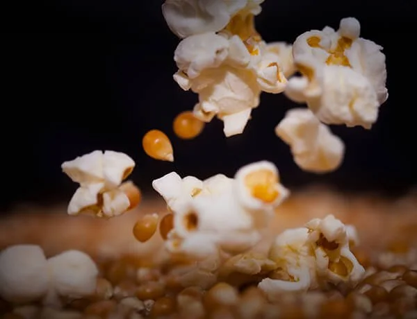 Close-up of popcorn and yellow popcorn kernels falling onto a surface.