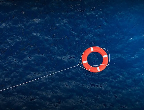 An orange and white life preserver floating in the water, tethered to a rope.